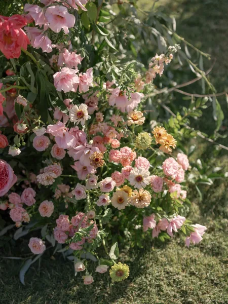 Wedding florals with garden wedding flowers in blush roses, pink and peach blooms, and greenery arranged on a sunlit grass lawn