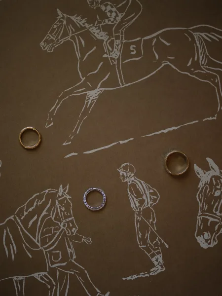 Wedding rings with gold wedding bands and a diamond eternity band arranged on illustrated paper with an equestrian sketch on brown background