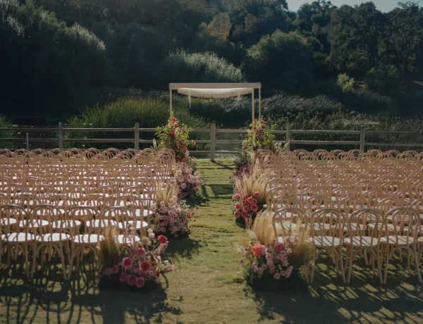 Ceremony setup with outdoor wedding ceremony chairs along a floral lined aisle, leading to a square arch with draped fabric by a pond