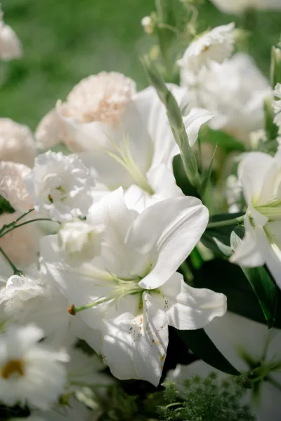 Bridal bouquet of white lilies with blush flowers and greenery on a green lawn in an outdoor garden setting