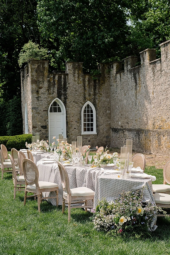 Outdoor reception tablescape with garden reception tables, patterned linens, pastel florals, bud vases and taper candles by stone wall arches
