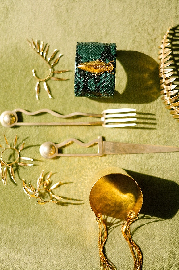 Wedding flatware with gold wedding flatware spoon, fork, and knife beside a napkin ring, styled on a green linen tablecloth