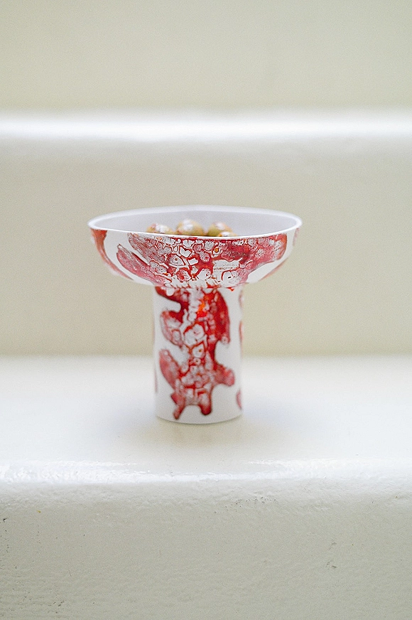 Wedding favors in a small ceramic bowl with red and white marbled glaze, filled with candy on a white ledge against a neutral wall