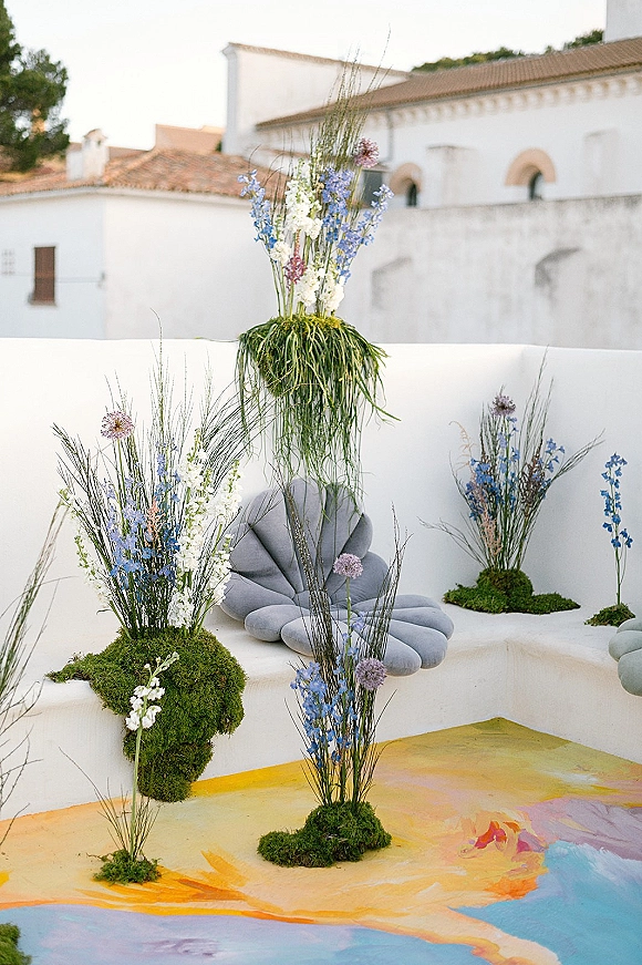 Wedding floral installation with a ceremony floral meadow of blue and white wildflowers and tall grasses against white stucco arches outdoors