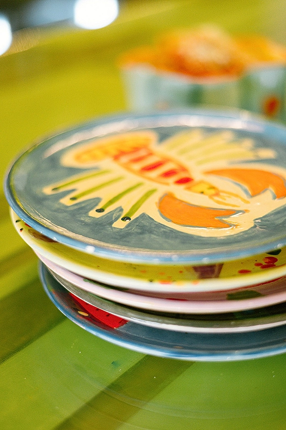Wedding place settings with stacked wedding plates and patterned dinnerware, featuring a lobster illustration plate on a green tablecloth with bokeh lights