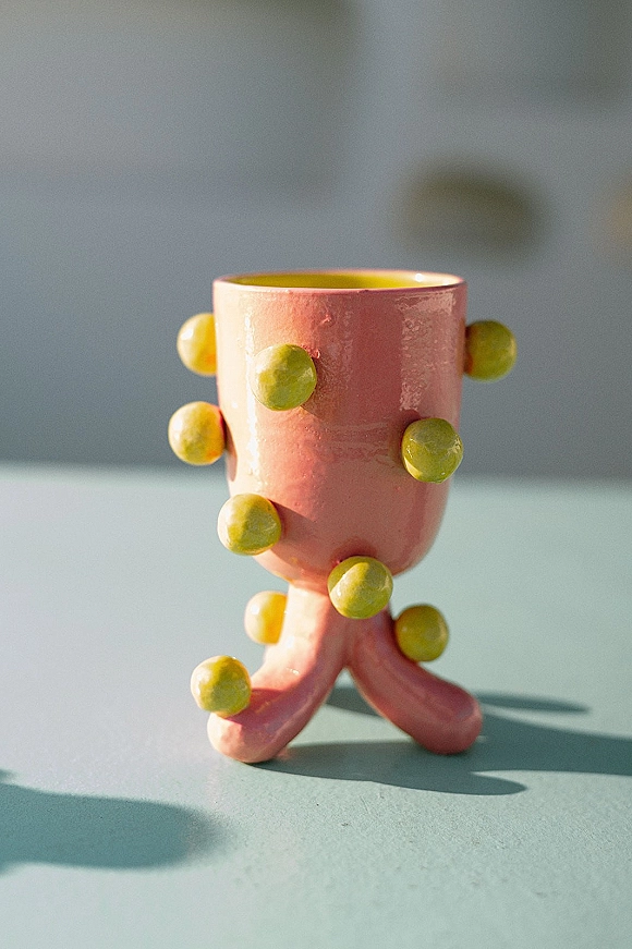 Wedding cake with pink fondant and green fondant balls, set on a pedestal stand against a gray backdrop on a tabletop surface