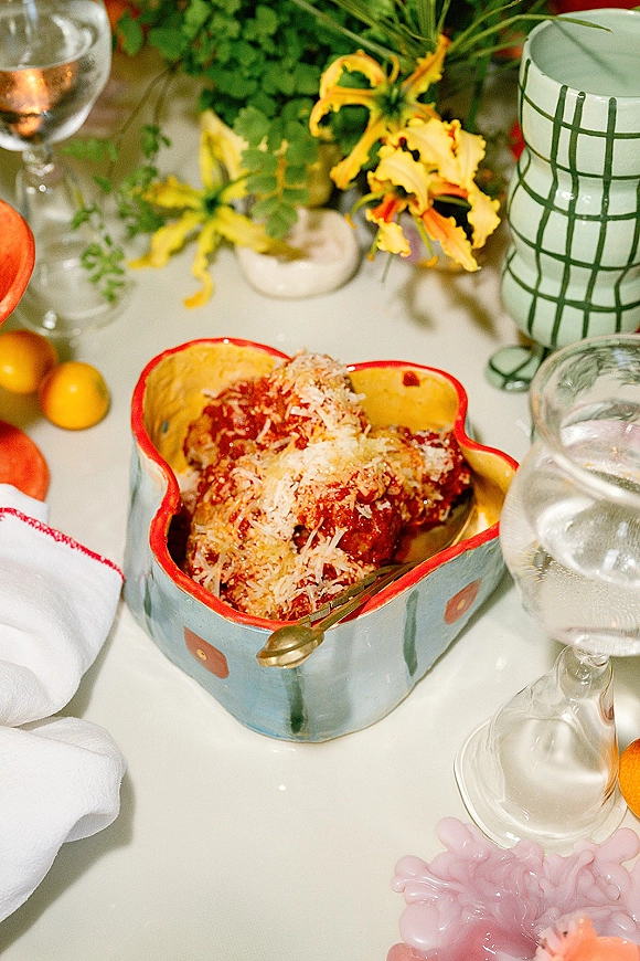 Wedding food pasta course served with meatballs in tomato sauce on a ceramic dish, fork and wine glasses on a white tabletop with lemons