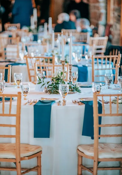 Reception tablescape with wedding table centerpiece of taper candles in brass candlesticks, greenery garland, and blue runner in a wooden hall