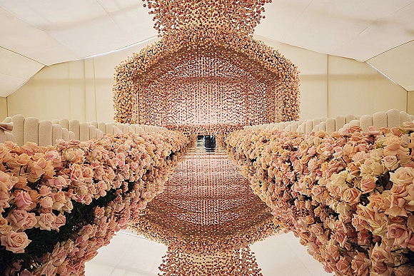 Ceremony aisle design with a floral lined wedding aisle of pink roses, mirrored runner, and a hanging flower installation under a tent ceiling