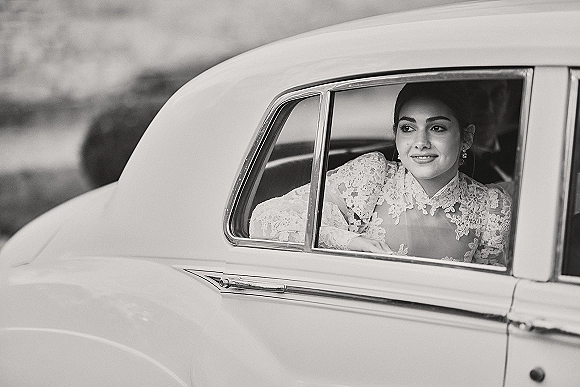 Bridal portrait of a bride in car, looking out the window in a lace wedding dress with bridal earrings, framed by vintage car interior