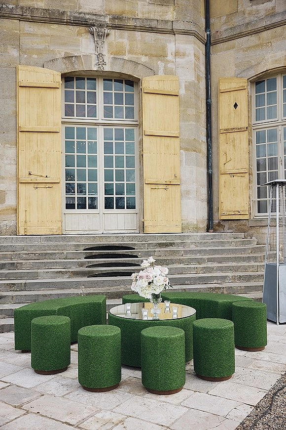 Wedding lounge area with a green curved sofa and ottomans around a mirrored coffee table with flowers and candles by French doors