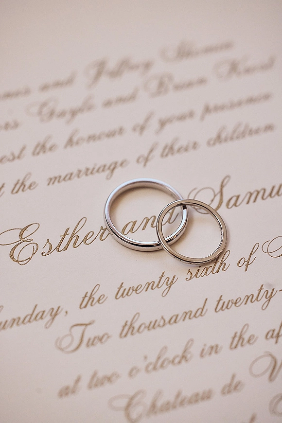 Wedding rings resting on a cream calligraphy invitation, wedding band close up showing engraved script on matching bands