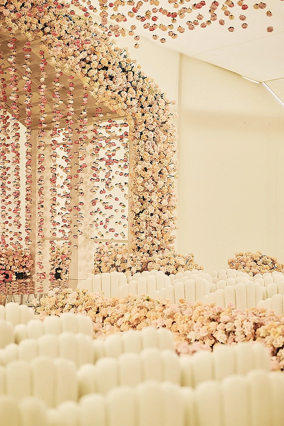 Ceremony floral installation with a wedding floral arch, hanging flower garlands, and blush rose aisle flowers in an indoor venue