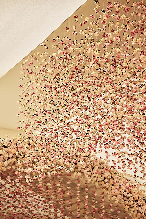 Hanging flower ceiling floral ceiling installation with cascading roses and garlands suspended on string lines beneath a white indoor venue ceiling
