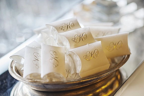 Wedding favor boxes with gold monogram labels and clear plastic spoons, styled in a silver serving bowl on a neutral tabletop