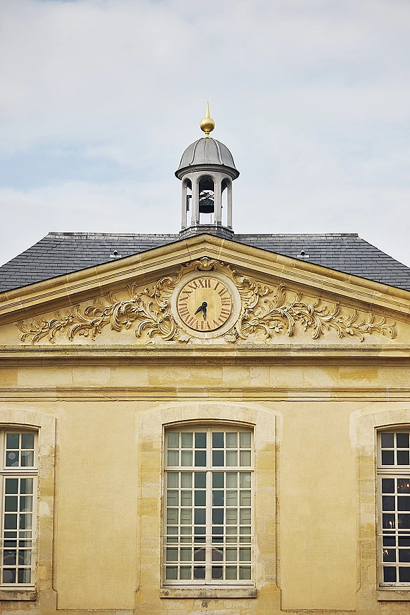 Wedding venue exterior of a historic wedding venue with a clock tower, ornate stone carvings, slate roof and windows against a pale sky