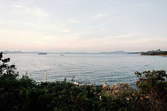 Ocean view venue with dock and railing overlooking the sea, boats, rocky shoreline, coastal shrubs, distant hills and sky