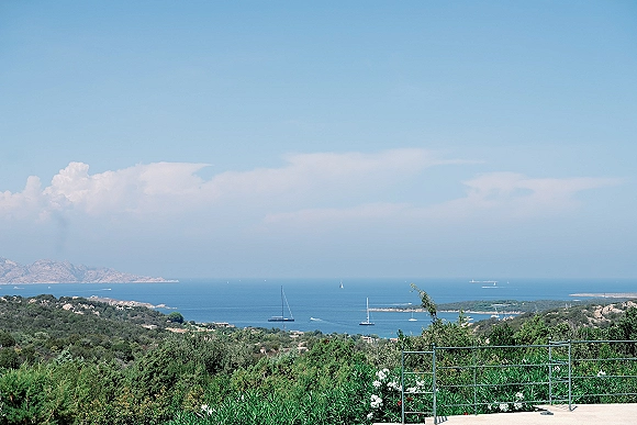 Ocean view landscape from a coastal overlook view, seen beyond a metal railing with sailboats on the sea under blue sky and clouds