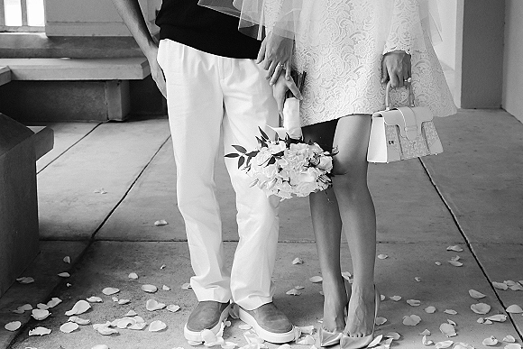 Couple portrait in a black and white wedding portrait style, holding hands on a concrete walkway with columns and steps behind them