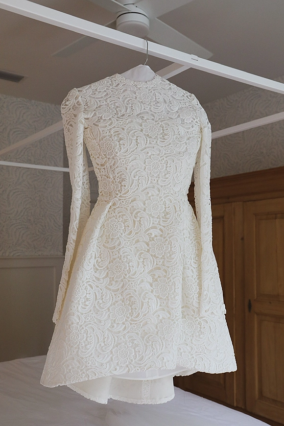Wedding dress with lace wedding dress details, long sleeves and high neck, hanging on a hanger in a bedroom with wooden wardrobe