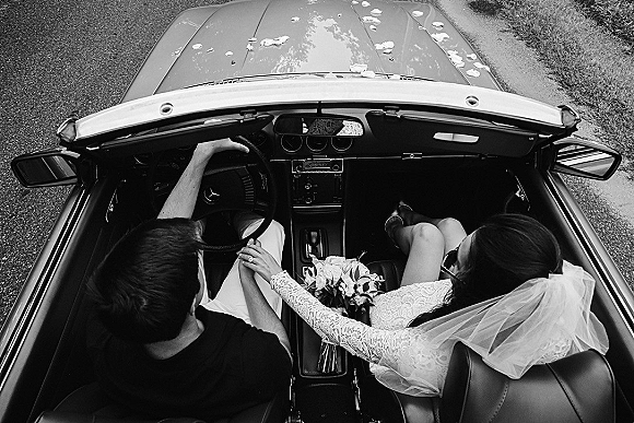 Wedding getaway car with bride and groom in car, overhead view of veil, lace sleeve, bouquet and rose petals on a roadside road
