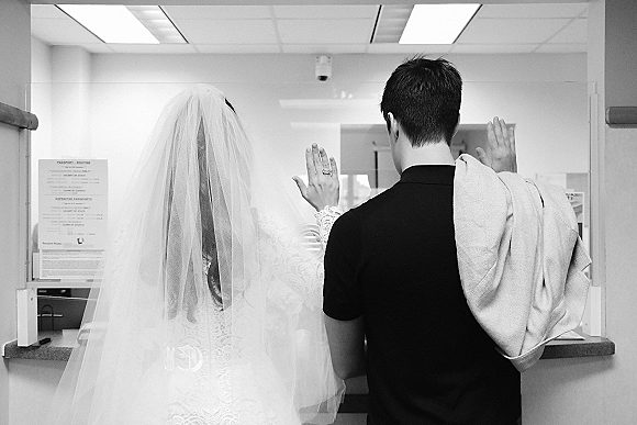 Courthouse wedding couple from behind, bride in veil and lace sleeves showing ring as groom holds jacket in office service counter setting
