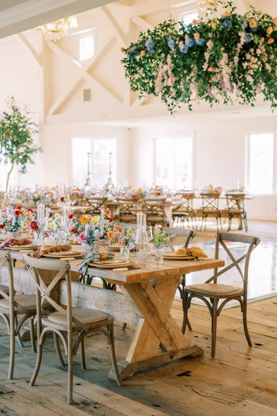 Reception tablescape at a farm table wedding reception featuring taper candles, set against shiplap walls with chandeliers and exposed beams.