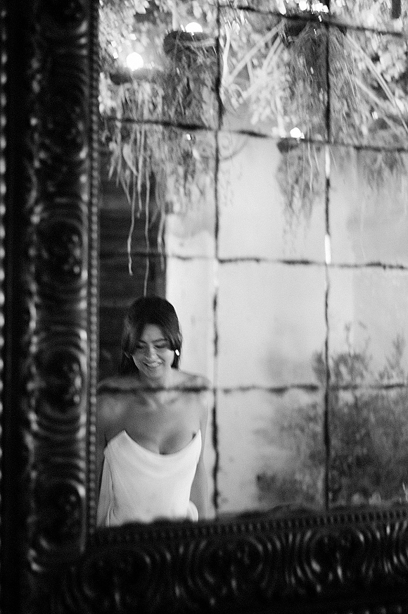 Bridal portrait of the bride in a black and white bridal portrait, seen in an ornate mirror with window light, greenery and string lights behind