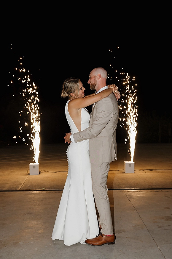 Wedding couple portrait with newlyweds embracing as cold spark fountains flare behind them on a concrete patio under the night sky