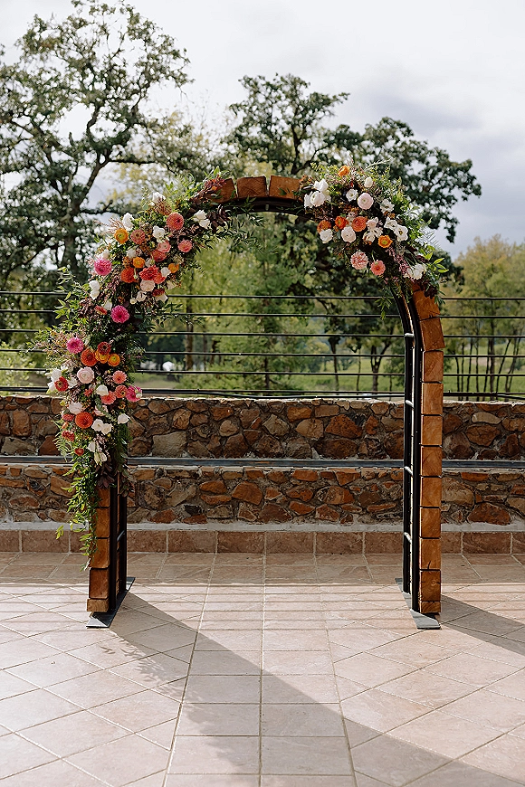 Wedding arch decor with floral wedding arch greenery garland and colorful blooms on a wooden-and-metal frame before a stone wall patio