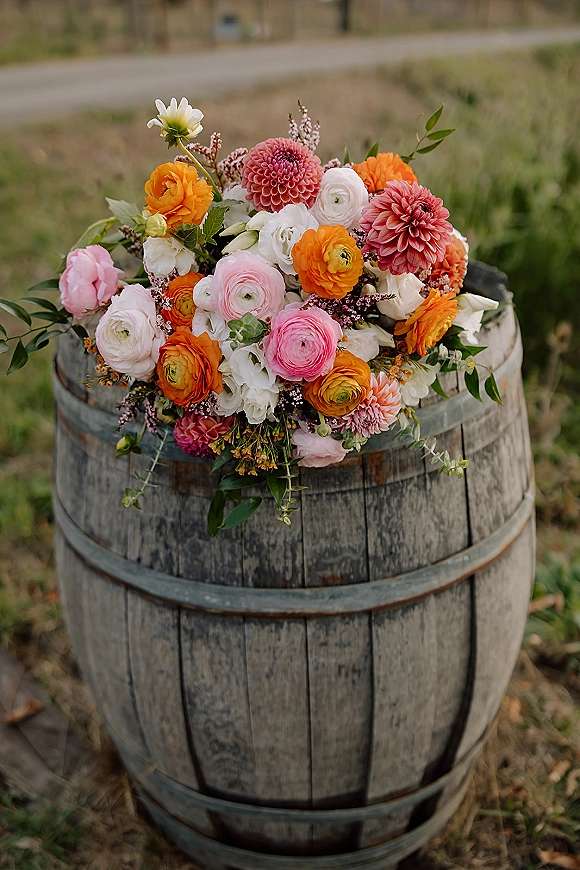 Bridal bouquet, bright wedding bouquet of dahlias and ranunculus with pink, orange, and white blooms on a wooden barrel outdoors