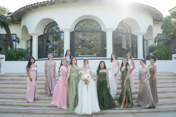 Bridesmaid group photo with bride with bridesmaids holding bouquets on a staircase, framed by stucco arches and palm trees with earrings accents