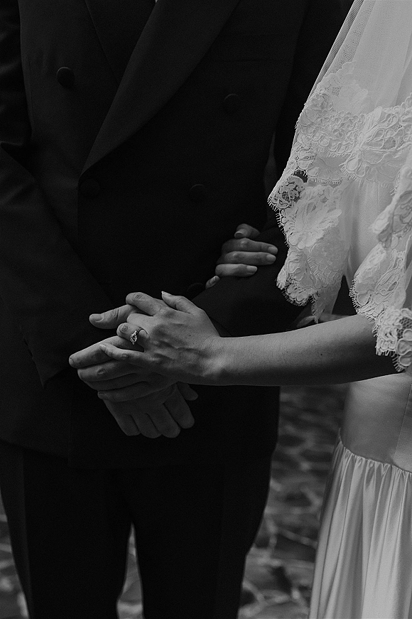 Wedding couple hands intertwined, bride holding groom arm with engagement ring and lace sleeves, walking along an outdoor path