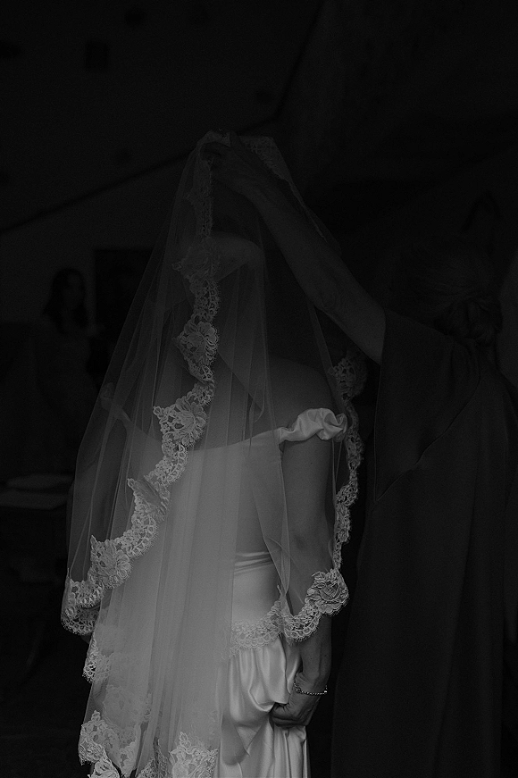 Wedding kiss as bride and groom share a kiss under a lace veil in a dark doorway, her off-shoulder dress and bracelet visible