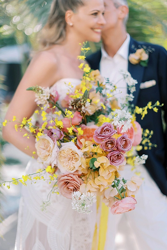 Bridal bouquet of garden rose bridal bouquet blooms in mauve, peach, white and yellow with greenery, held by bride outdoors in sunlight