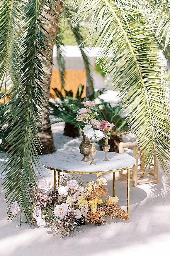 Wedding lounge decor with wedding cocktail lounge styling, featuring a round marble coffee table with brass vases and roses on a sunlit patio with palm trees
