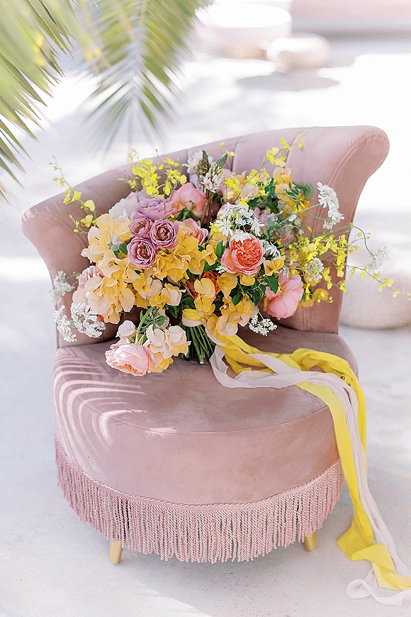 Bridal bouquet, colorful bridal bouquet with roses, hydrangea, ranunculus and greenery, draped in silk ribbons on a pink velvet chair on a sunlit patio