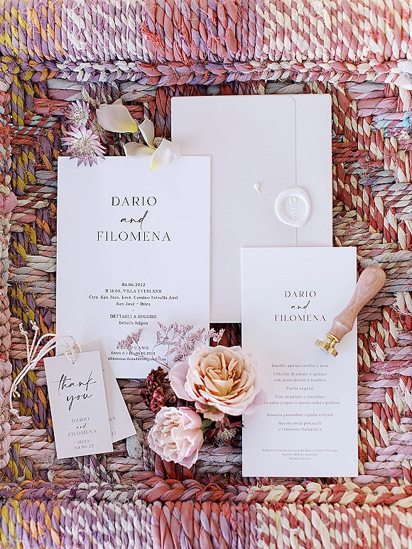 Wedding invitation suite with modern wedding invitations, envelope and wax seal accented by dried roses on a woven braided rug flat lay