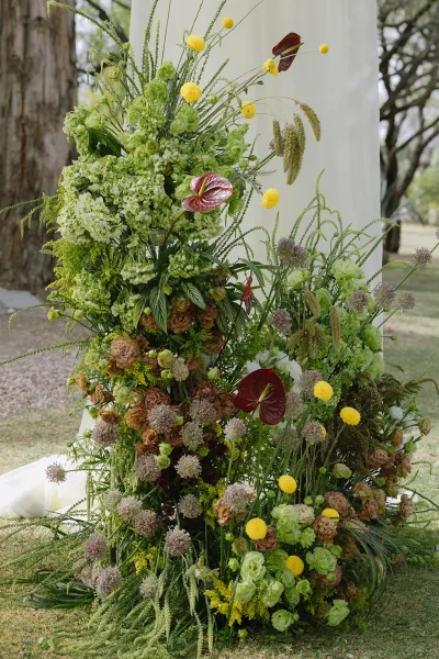 Ceremony floral installation with wedding ceremony flowers, lush greenery, hydrangea and anthurium on draped backdrop on a lawn outdoors