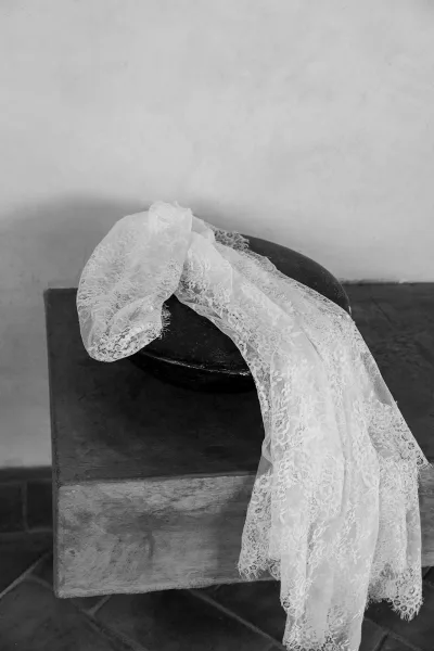 Lace veil with mantilla lace veil edging draped over a round stool on a stone pedestal against a plaster wall and tiled floor