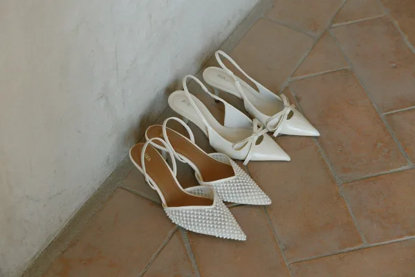 Bridal shoes, pearl wedding shoes in slingback pointed-toe heels with bows, arranged on terracotta tile floor by a plaster wall