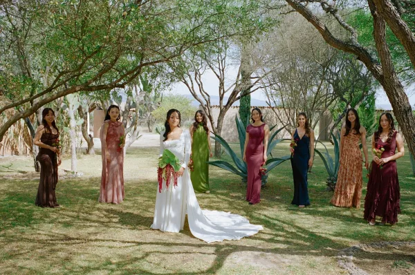 Bride with bridesmaids posing in a garden, bride centered in long sleeve gown with train, bridesmaid dresses and bouquets among agave plants