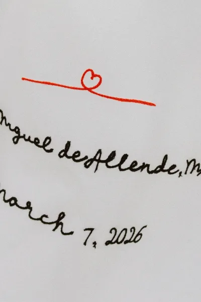 Wedding invitation with handwritten wedding invitation calligraphy in black ink, featuring a small red heart doodle on white paper