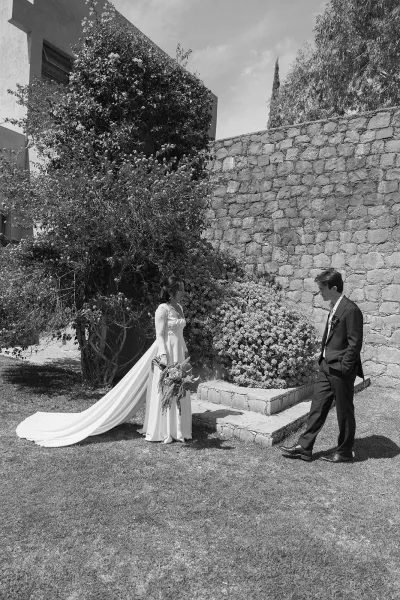Couple portrait in a black and white wedding portrait, bride holding bouquet with long train beside groom in dark suit by stone wall steps outdoors