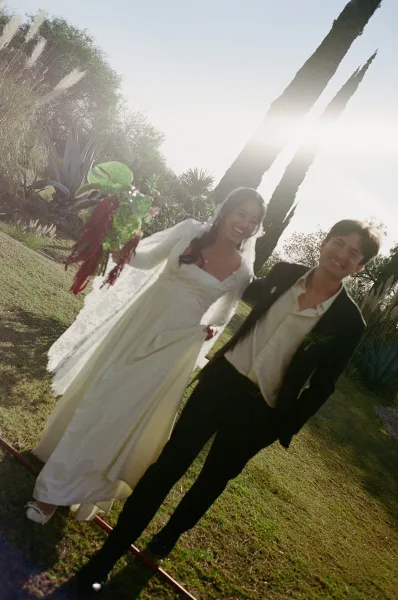 Couple portrait of bride and groom walking on a sunny garden lawn, her veil and bouquet flowing as he wears a black suit and boutonniere