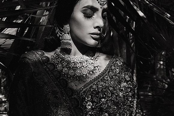 Bridal portrait in black and white showing side profile with maang tikka and jhumka earrings, palm leaf shadows across her face