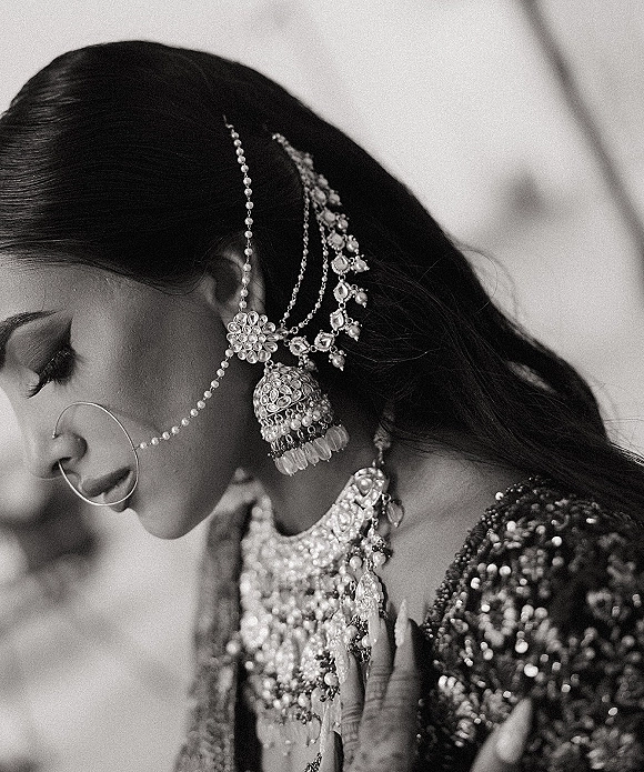 Bridal jewelry close up featuring a bridal nose ring with maang tikka, jhumka earrings, and choker necklace against a soft indoor backdrop