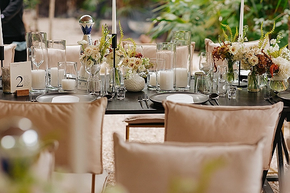 Reception tablescape with modern wedding table decor, taper candles and low florals on a black table set on an outdoor patio with greenery