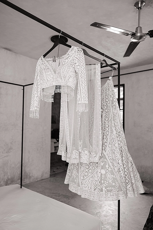 Wedding dress and lace wedding dress hanging on a clothing rack, showing beaded fringe sleeves and a sheer veil in a bedroom