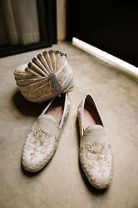 Groom accessories flatlay with embroidered loafers and wedding turban, gold embroidery and jeweled brooch on concrete by dark doorway